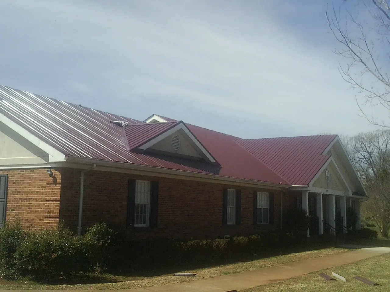 Red metal roof with gabled entries on a long brick building, from a Hail Damage Roof Repair job in Birmingham