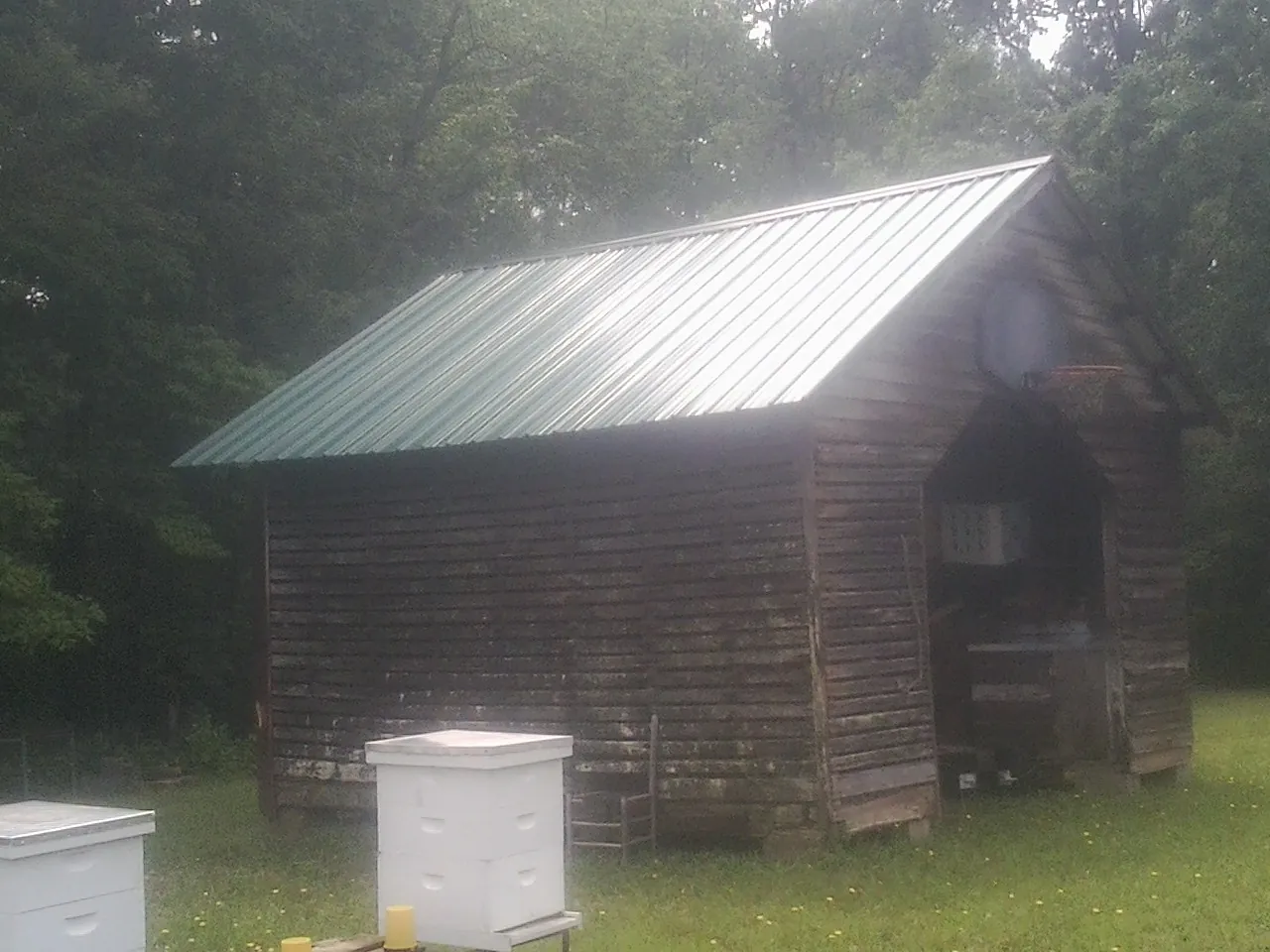 Green metal roof on a weathered barn beside stacked beehives in Birmingham