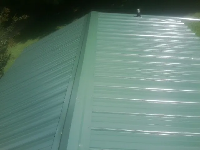 New green metal panels meeting at the ridge of a roof — Flat Roof Repair work by our crew in Birmingham